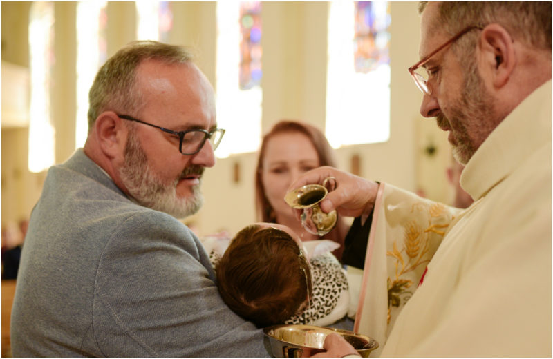 chrzest portret chrzest mała dziewczynka z wiankiem na głowie siedzi pod magnolią