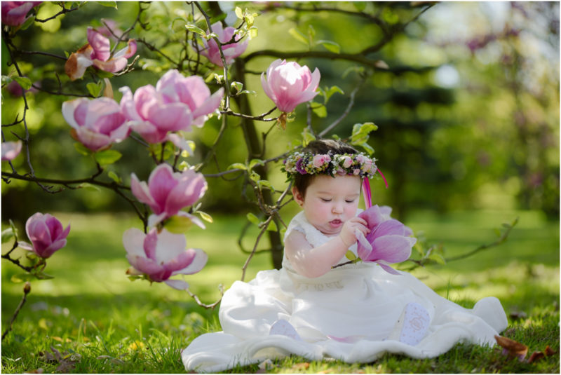 chrzest portret chrzest mała dziewczynka z wiankiem na głowie siedzi pod magnolią