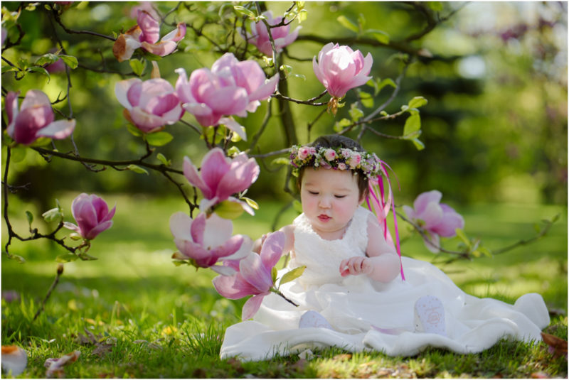 chrzest portret chrzest mała dziewczynka z wiankiem na głowie siedzi pod magnolią