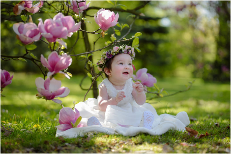 chrzest portret chrzest mała dziewczynka z wiankiem na głowie siedzi pod magnolią