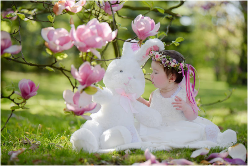 chrzest portret chrzest mała dziewczynka z wiankiem na głowie siedzi pod magnolią